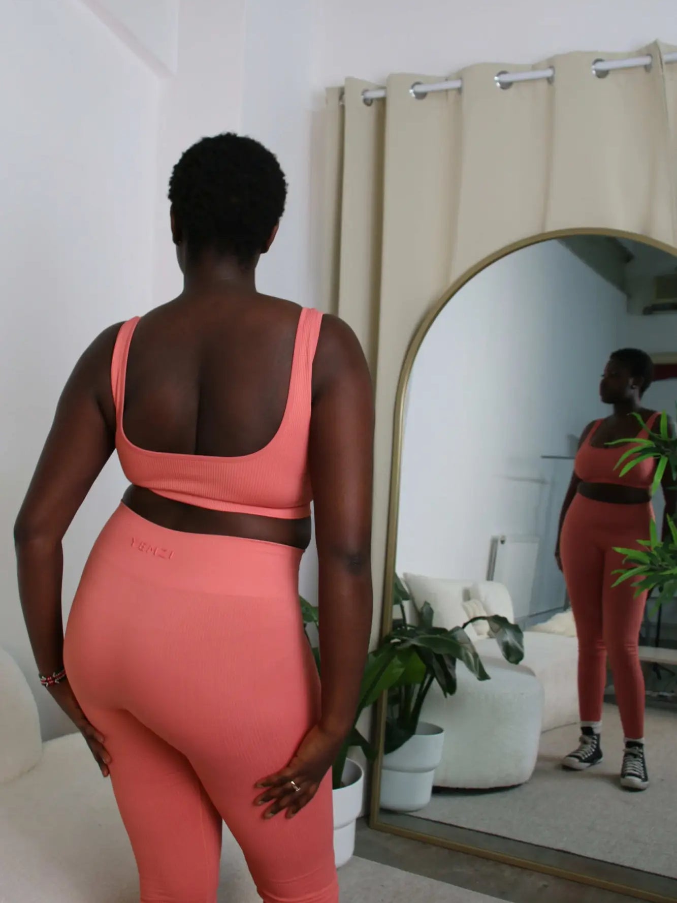 back view of plus size model in guava active ribbed set looking in the mirror