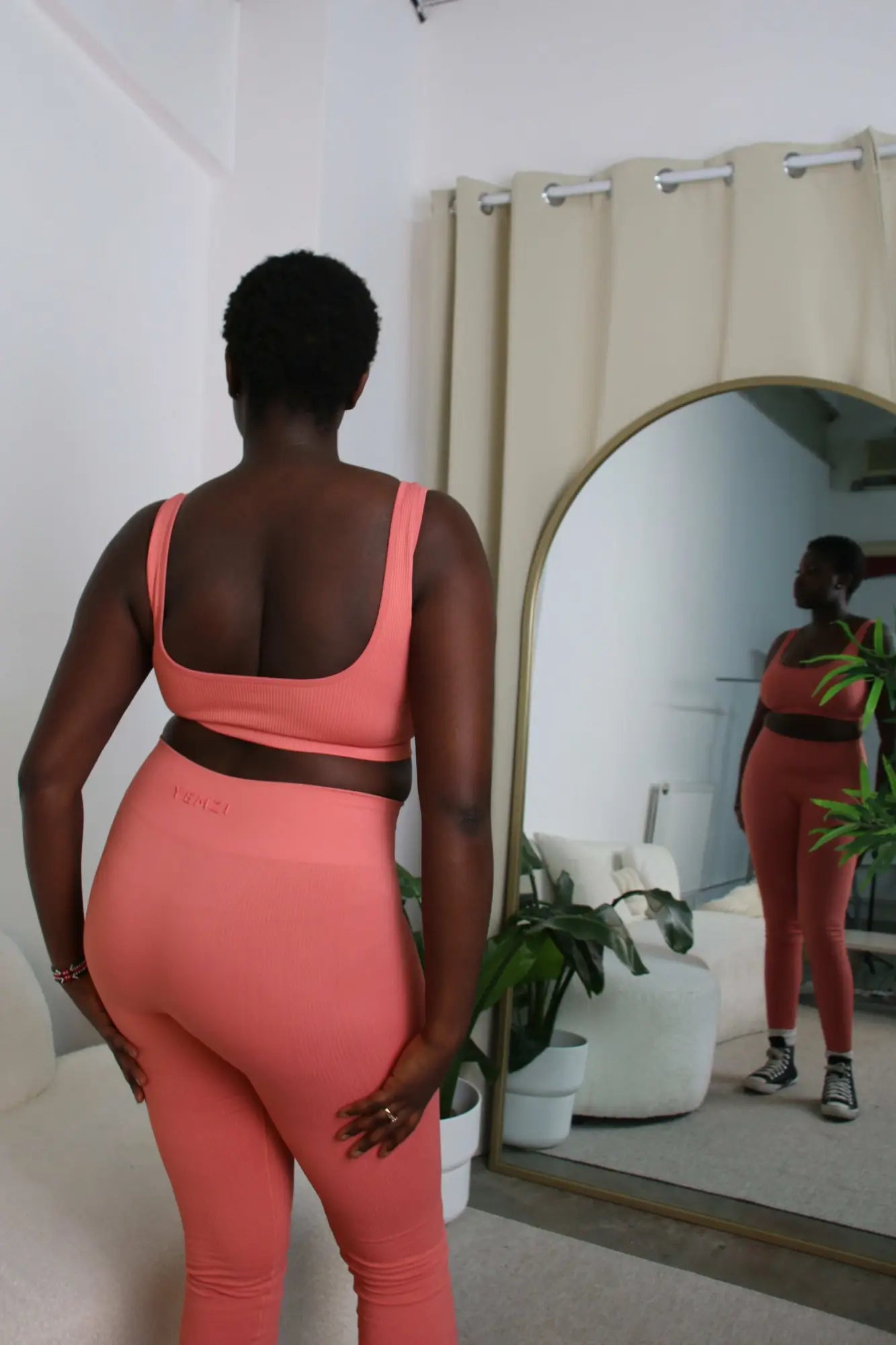 back view of plus size model in guava active ribbed set looking in the mirror