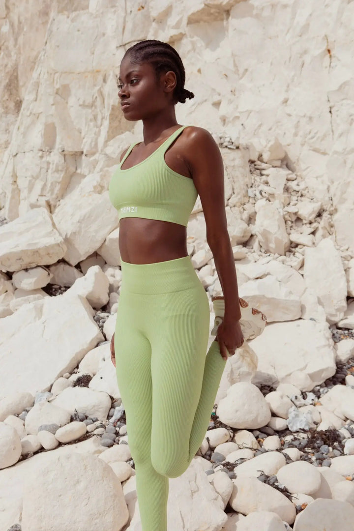 dark skin model walking and stretching by the seaside cliffs in a green activewear set