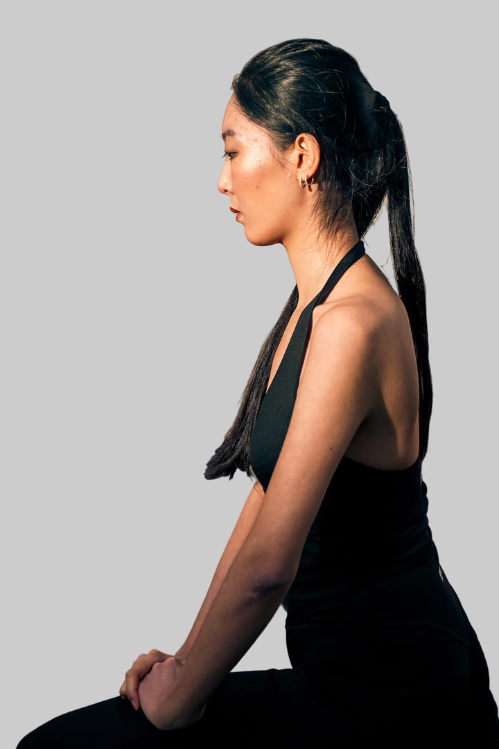Woman in black outfit sitting on stone steps with a blurred reflection in the mirror.