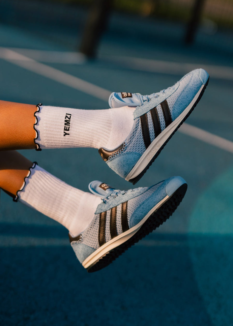 Blue sneakers with black stripes worn on a tennis court