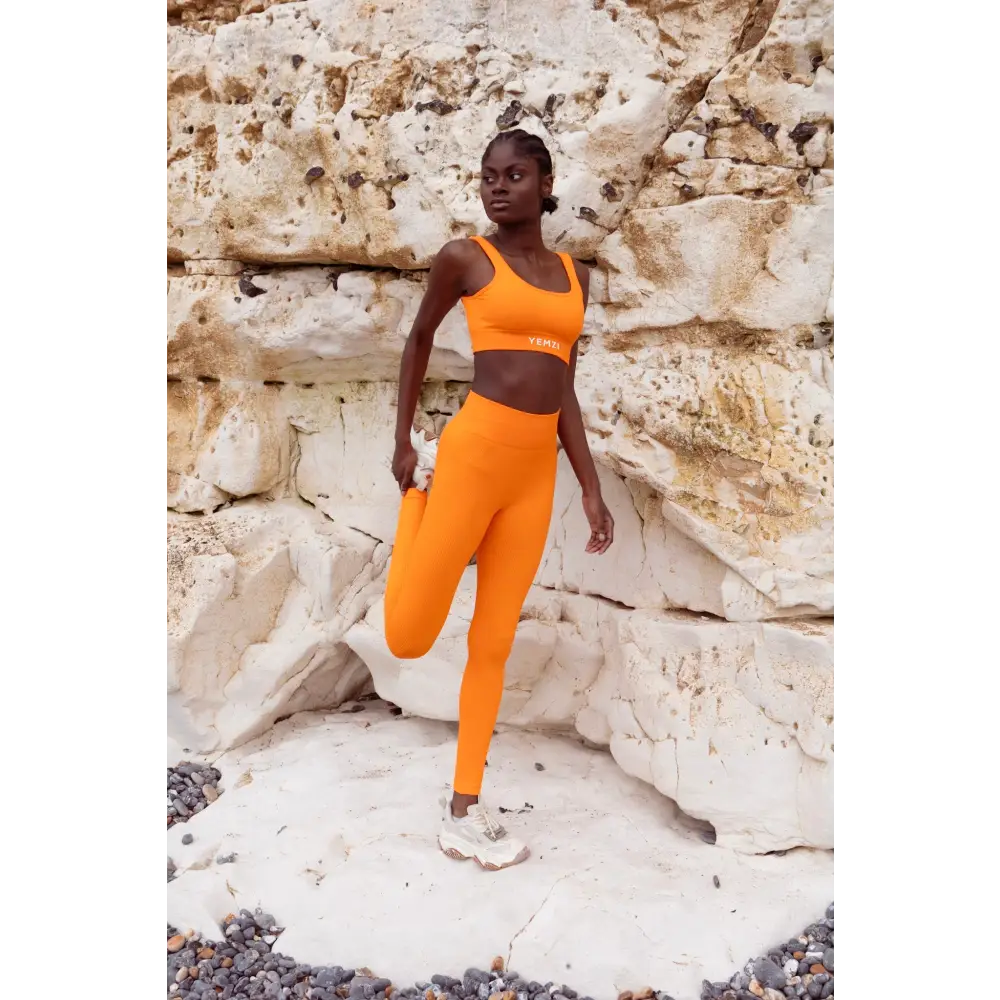 Model wearing Yemzi Orange fanta ribbed two piece leggings bra activewear set in rocky outdoor location - stretch