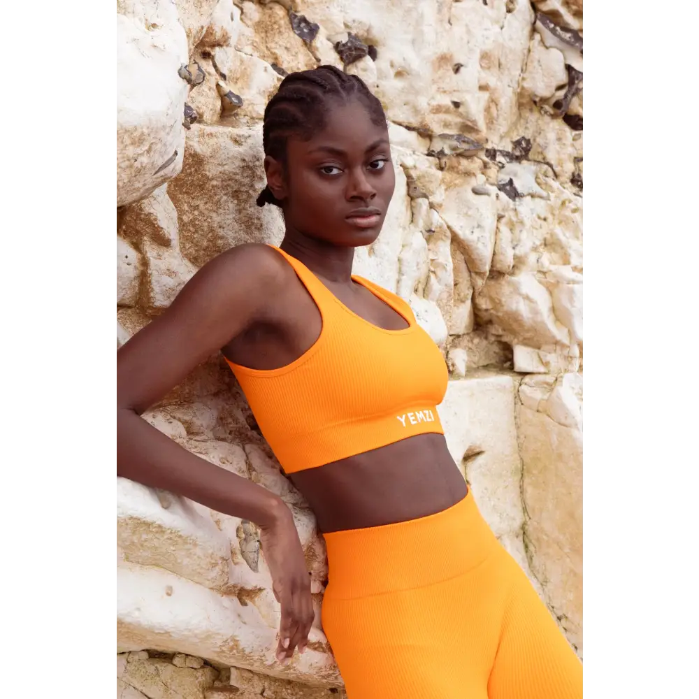 Model wearing Yemzi orange fanta ribbed activewear set in rocky outdoor location