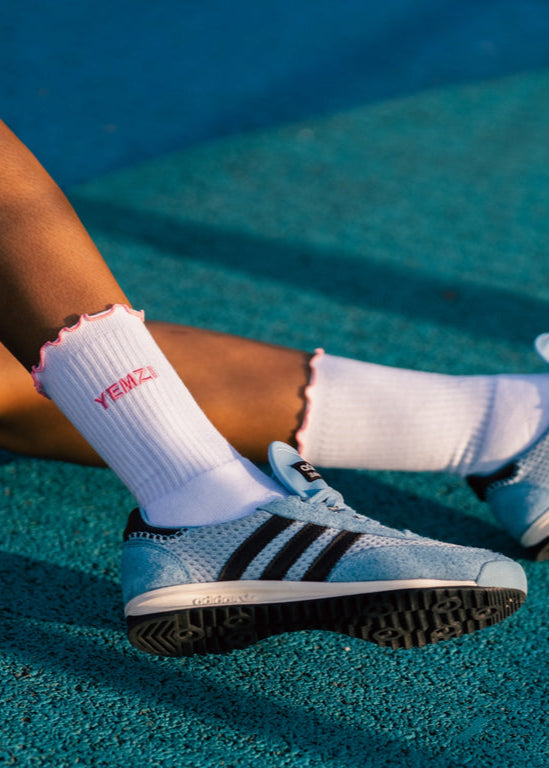 brown lady wearing Adidas shoes and white socks with pink details on a tennis court