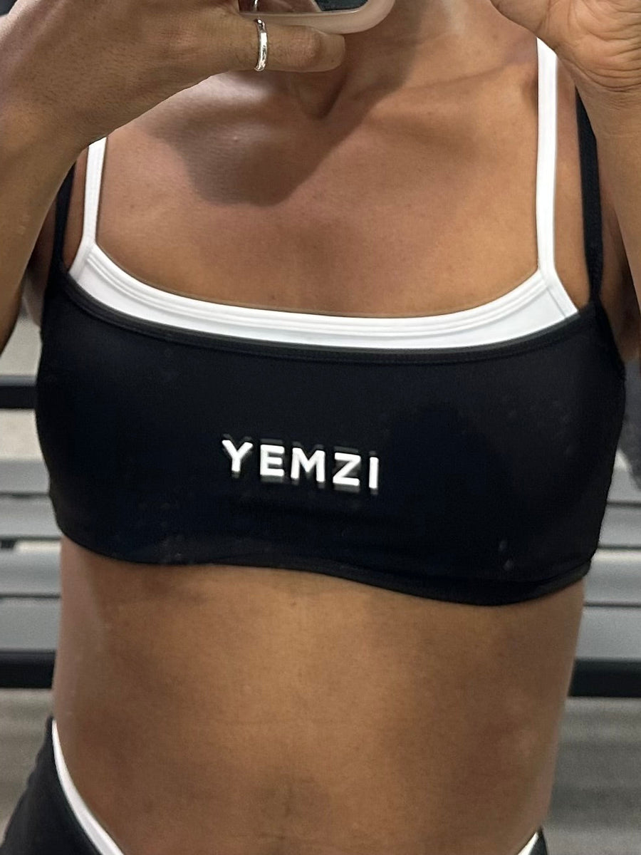 Black sports bra with white logo worn by a person, on a neutral background