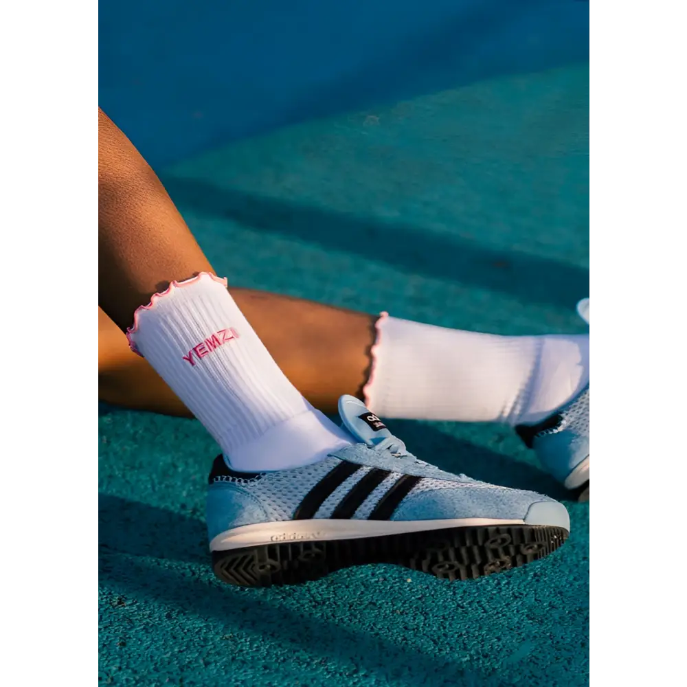 brown lady wearing Adidas shoes and white socks with pink details on a tennis court