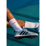 brown lady wearing Adidas shoes and white socks with pink details on a tennis court