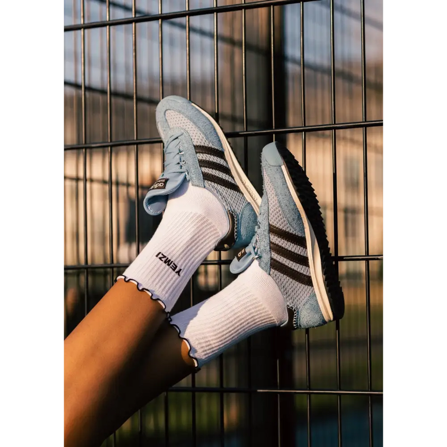Person wearing blue and gray sneakers with white socks against a metal fence background