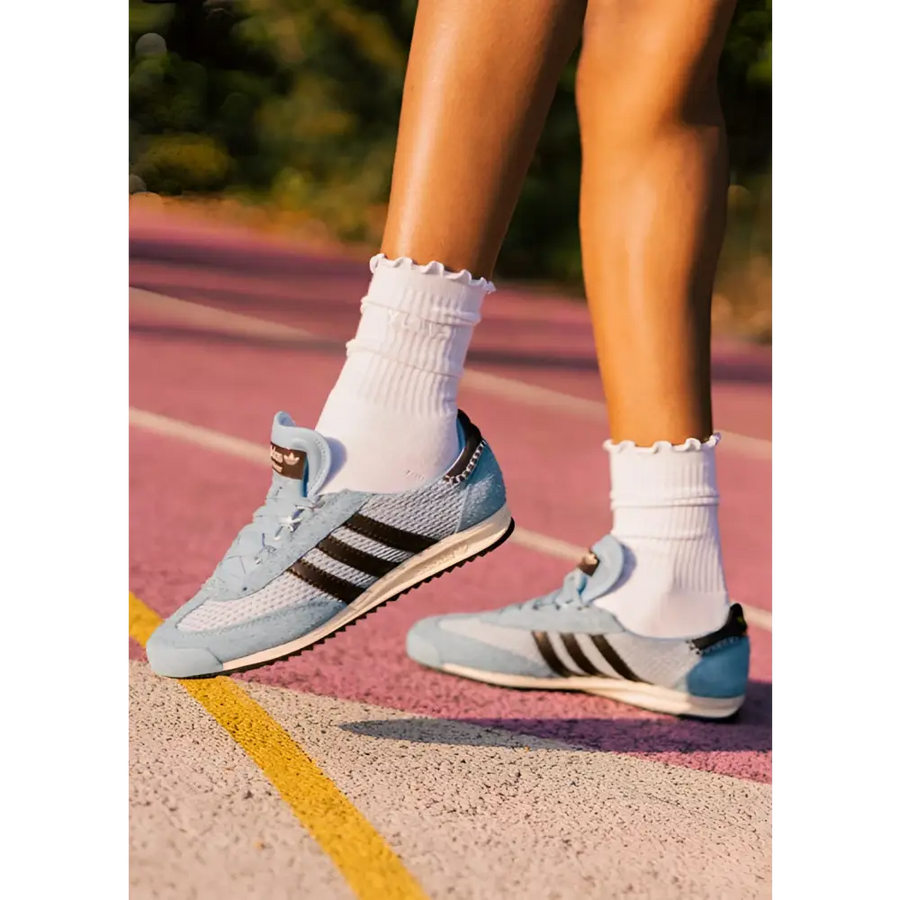 Person wearing light blue Adidas sneakers on a running track