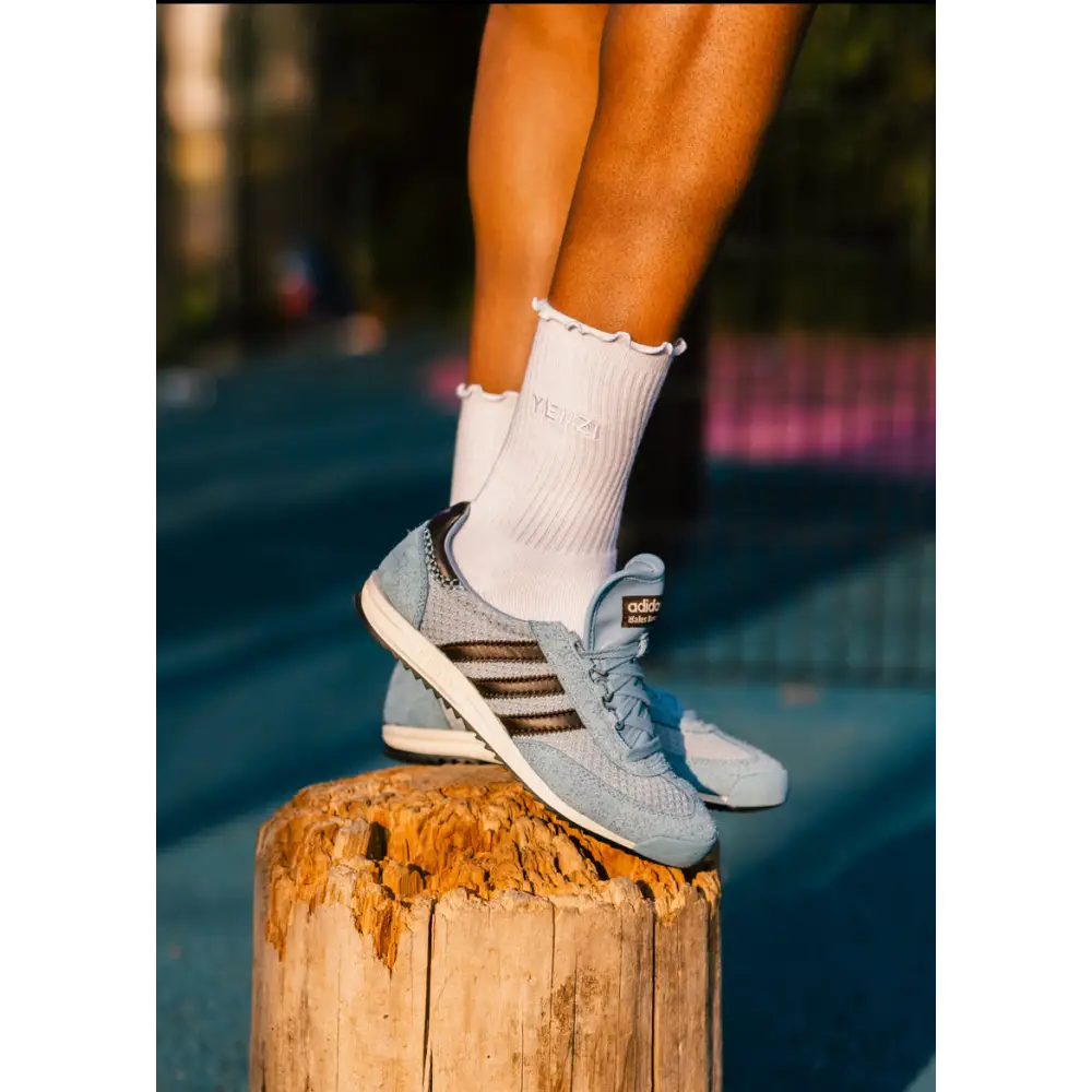 Person wearing light blue sneakers with brown stripes and white socks, standing on a wooden post.