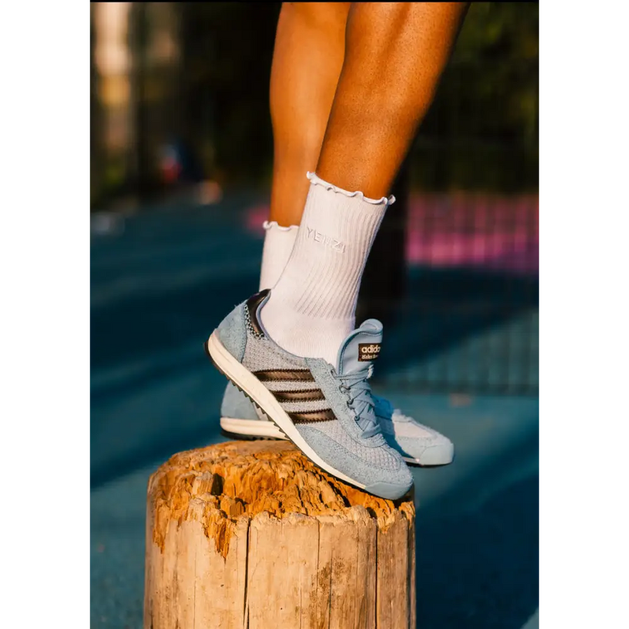Person wearing light blue sneakers with brown stripes and white socks, standing on a wooden post.