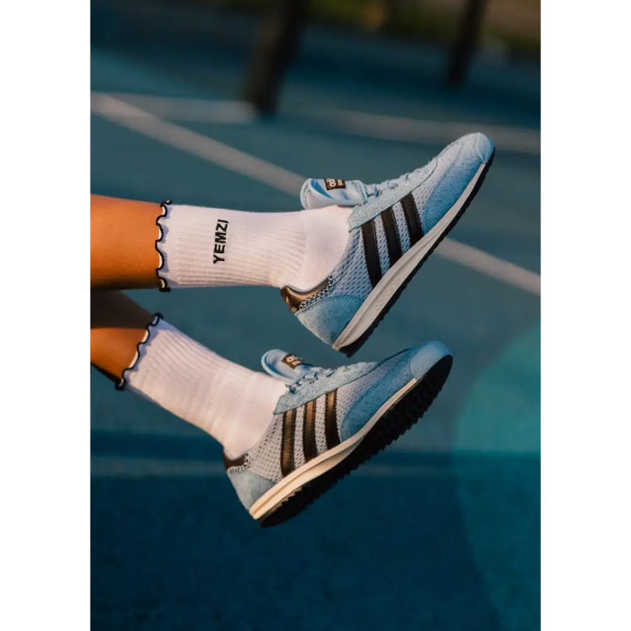 Blue sneakers with black stripes worn on a tennis court