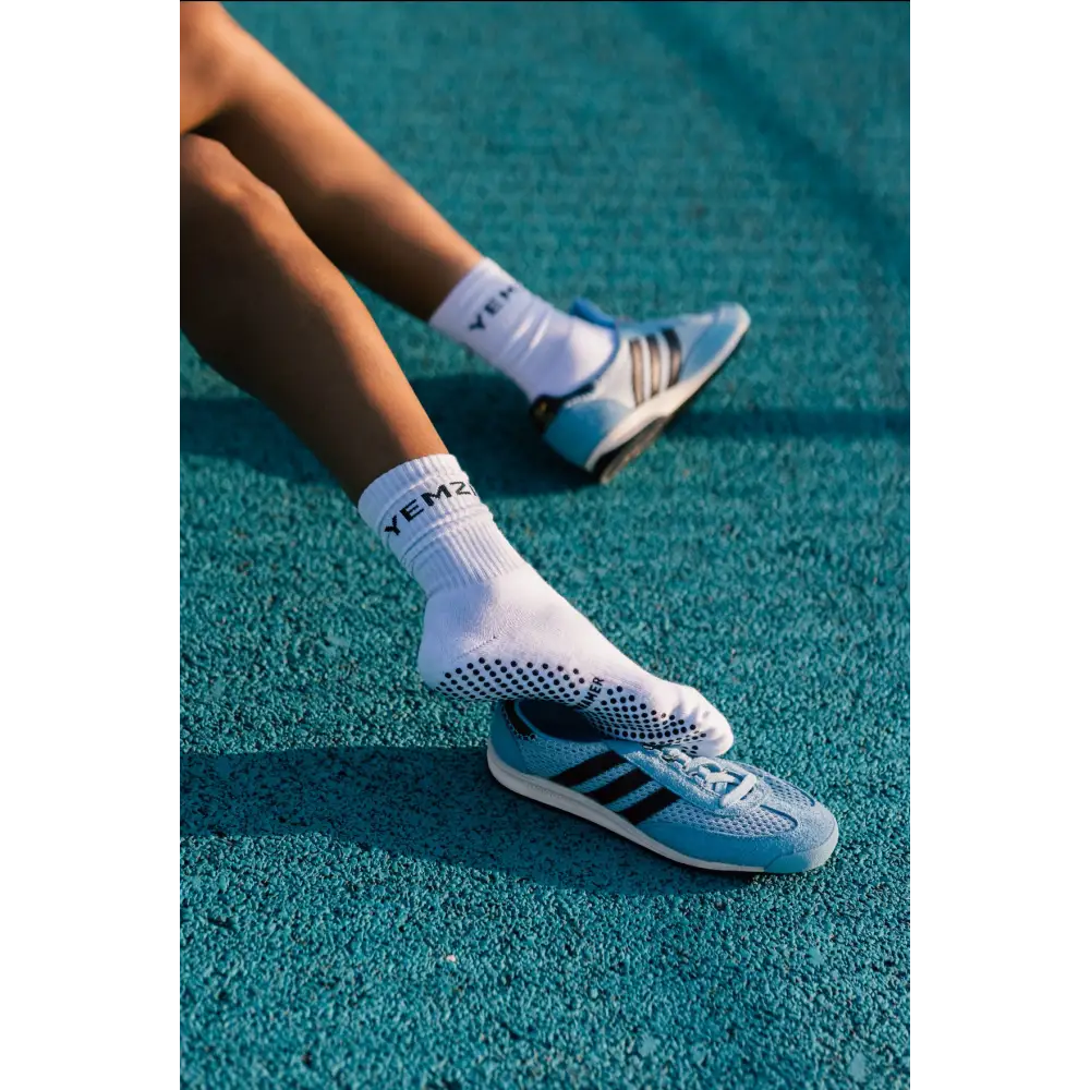 Person wearing white socks with black bold dreamer text and Adidas shoes on a blue track surface