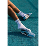 Person wearing white socks with black bold dreamer text and Adidas shoes on a blue track surface
