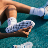 brown lady wearing white sneakers with black stripes on a blue track