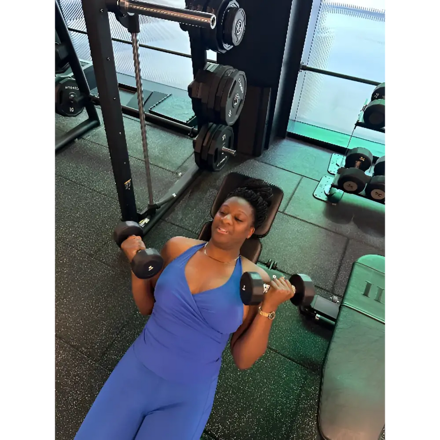 Woman in a blue dress exercising with dumbbells in a gym setting