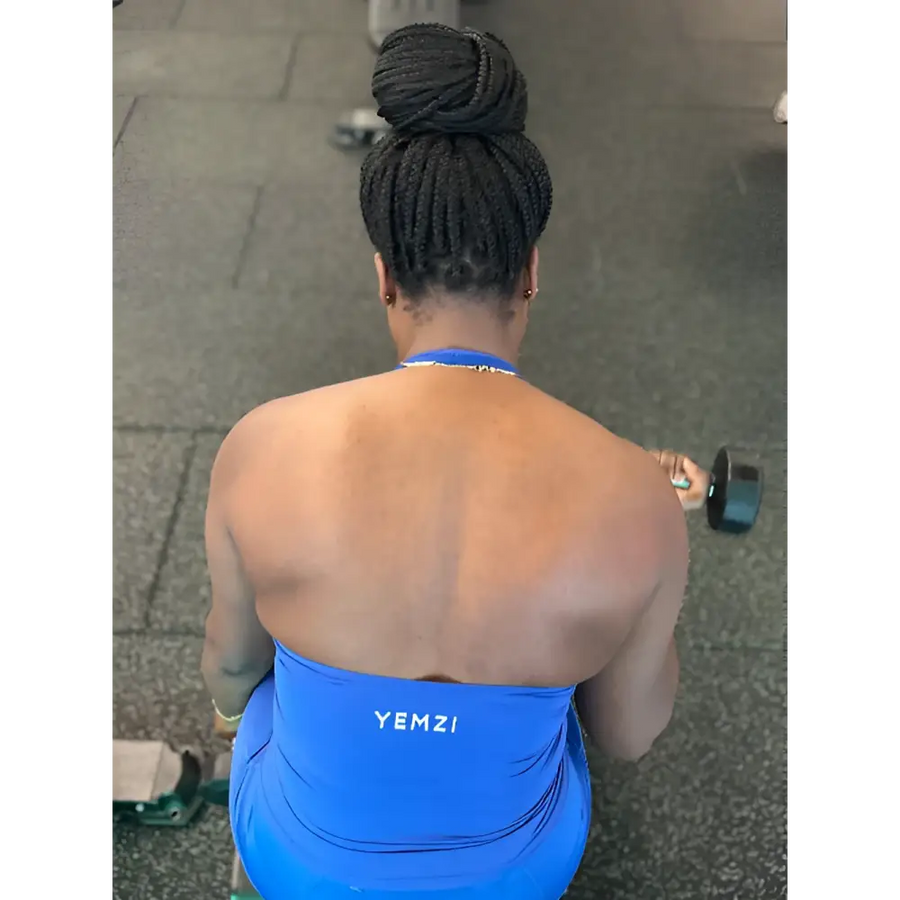 Lady in a blue 'YEMZI' tank top lifting a dumbbell outdoors.