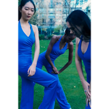 Three women in blue outfits standing on a grassy area with trees and buildings in the background.