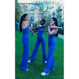 Three women in matching blue outfits standing on a grassy area with buildings in the background.