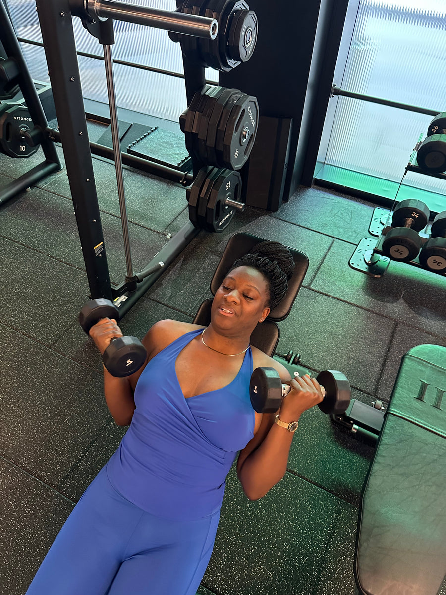 Woman in a blue dress exercising with dumbbells in a gym setting