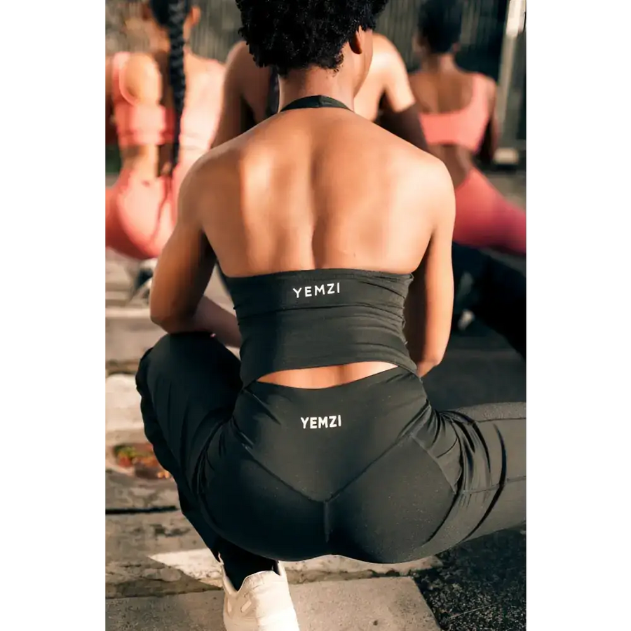 Person wearing black YEMZI athletic wear sitting on a stone surface.