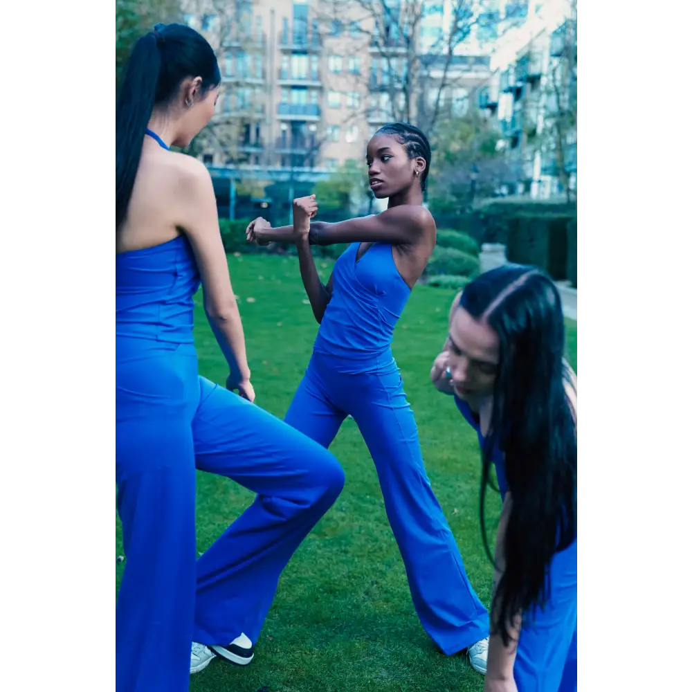 Three women in blue outfits practicing martial arts on a grassy area with buildings in the background.
