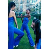 Three women in blue outfits practicing martial arts on a grassy area with buildings in the background.