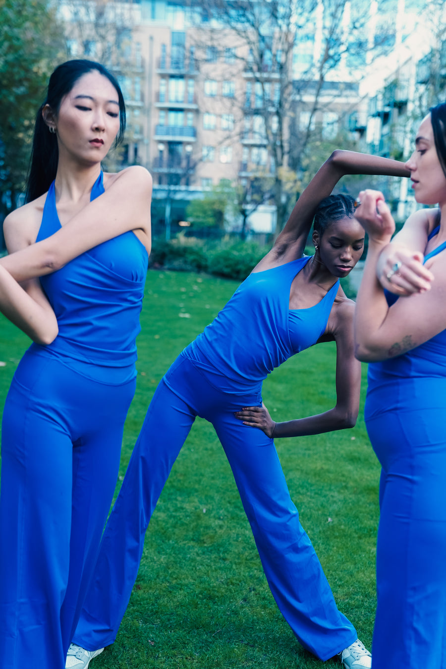 Three women in blue athletic wear posing outdoors with a cityscape background