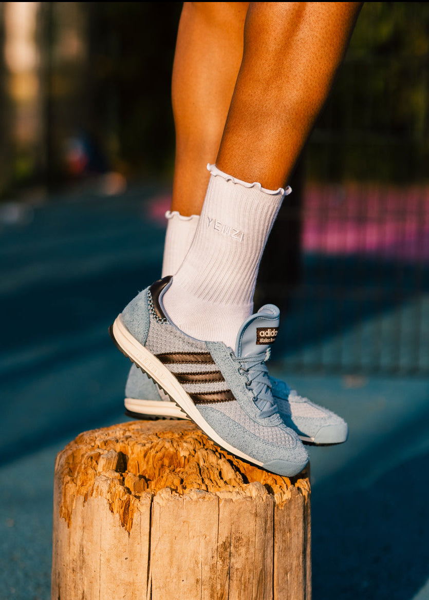 Person wearing light blue sneakers with brown stripes and white socks, standing on a wooden post.