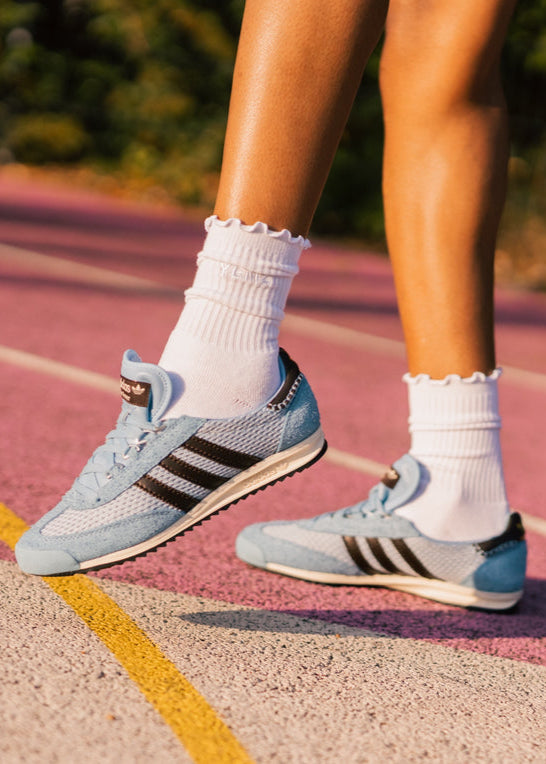 Person wearing light blue Adidas sneakers on a running track