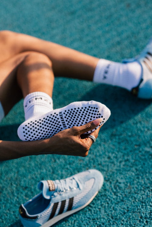 brown lady wearing white sneakers with black stripes on a blue track