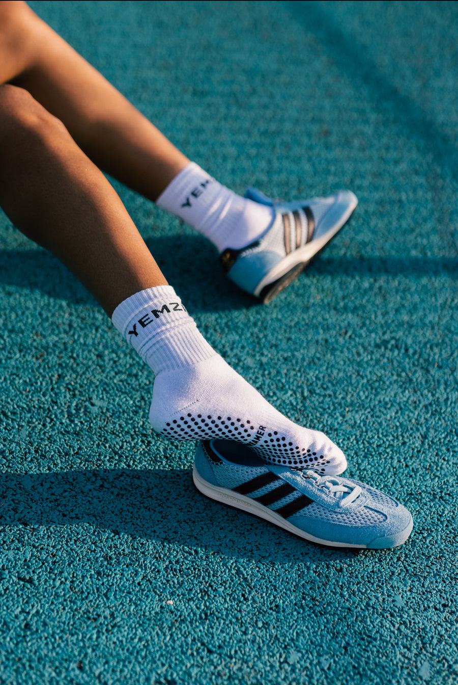 Person wearing white socks with black bold dreamer text and Adidas shoes on a blue track surface