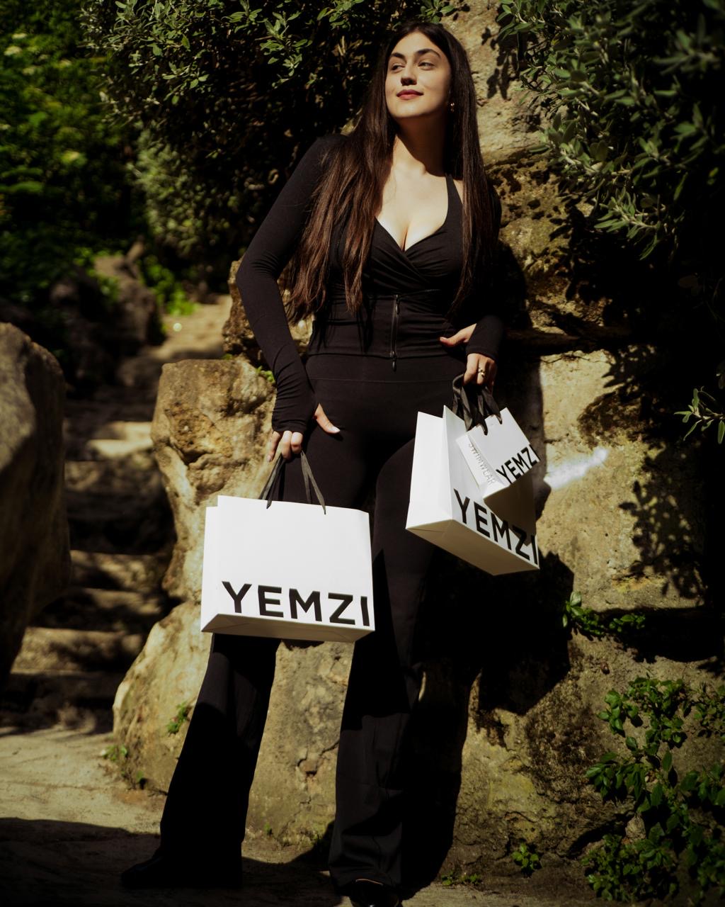 Woman holding YEMZI shopping bags in an outdoor setting